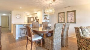 A dining area with wicker chairs, a round table, and a hanging light fixture. - Ocean One 315 - Oceanfront 3rd Floor Condo (Hilton Head Island)