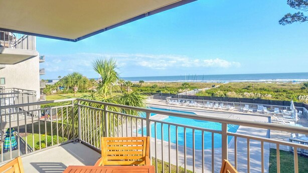 A balcony with a pool, wooden furniture, and a view of the beach and ocean. - Ocean One 315 - Oceanfront 3rd Floor Condo (Hilton Head Island)