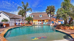 Une piscine à thème tropical, entourée de palmiers et bordée d’un bâtiment à la façade jaune.