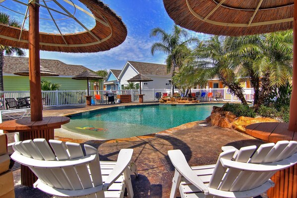 A pool area with lounge chairs, umbrellas, and a clear view of the pool. - This unit offers a fabulous slope entry pool, gas BBQ grills and is close to man (Port Aransas)