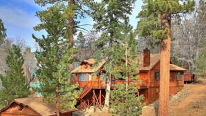 A log cabin with a garage, a deck, and a staircase leading to a second level. - Columbine Oak Retreat- Log Style Cabin W/ Spa (Big Bear City)