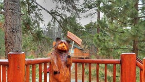 A wooden bear statue on a wooden platform with a 'GO AWAY' sign, surrounded by a wooden railing and trees. - Columbine Oak Retreat- Log Style Cabin W/ Spa (Big Bear City)