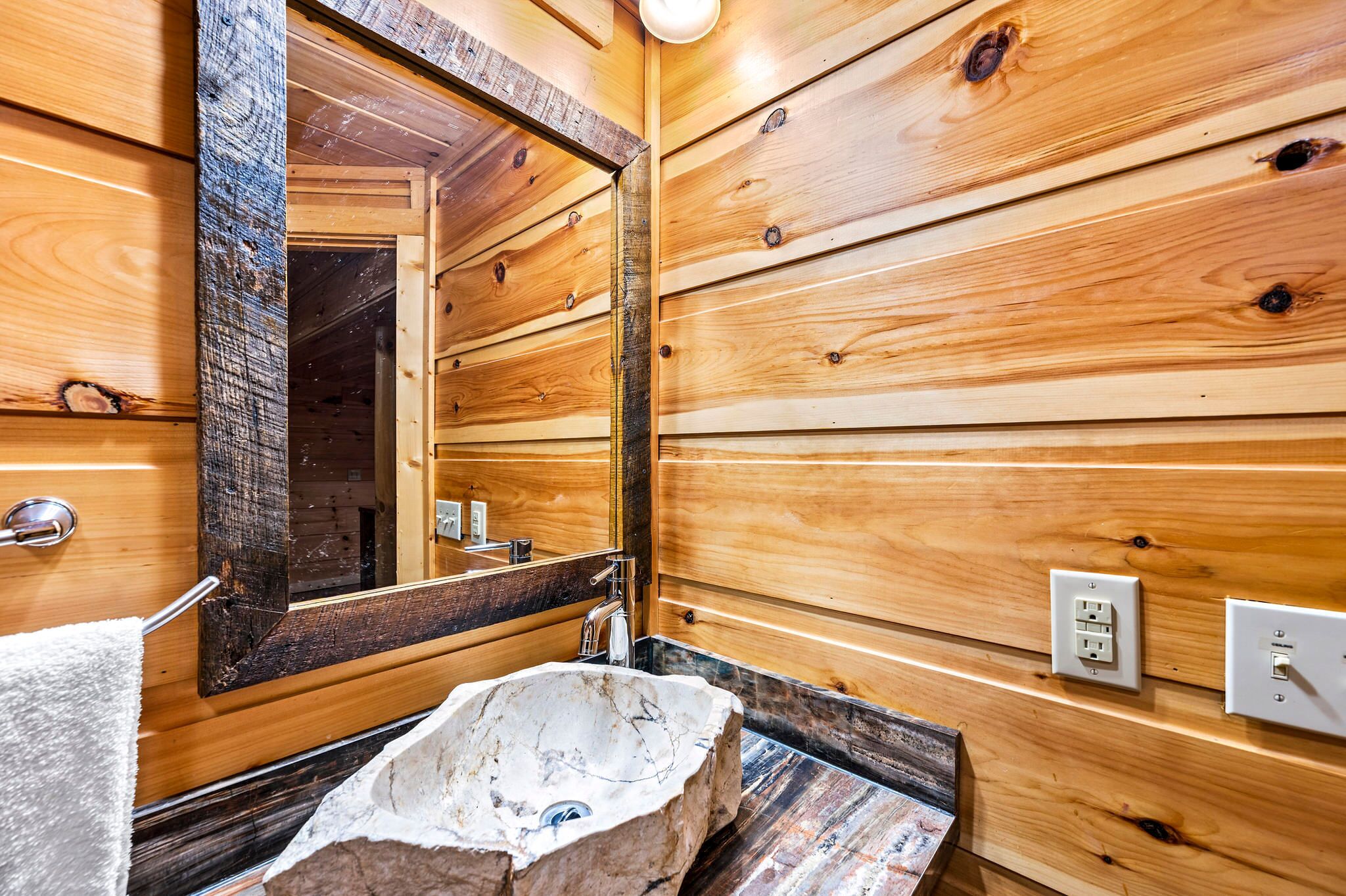 Un baño de cabaña de madera con un espejo grande, un lavabo de piedra y paredes de madera.