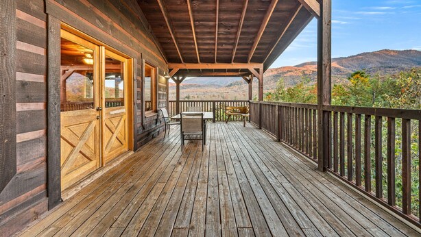 A wooden deck with a covered area, a table, and chairs, overlooking a mountainous landscape. - Take My Breath Away: Mountain Views, Theater (Gatlinburg)