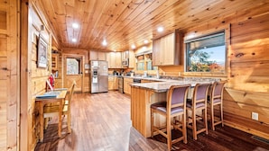 A wooden cabin interior with a kitchen, dining area, and large windows. - Take My Breath Away: Mountain Views, Theater (Gatlinburg)