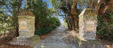 A stone pathway leading to a beach, flanked by stone pillars with signs indicating no vehicles allowed and neighborhood pedestrian beach access.