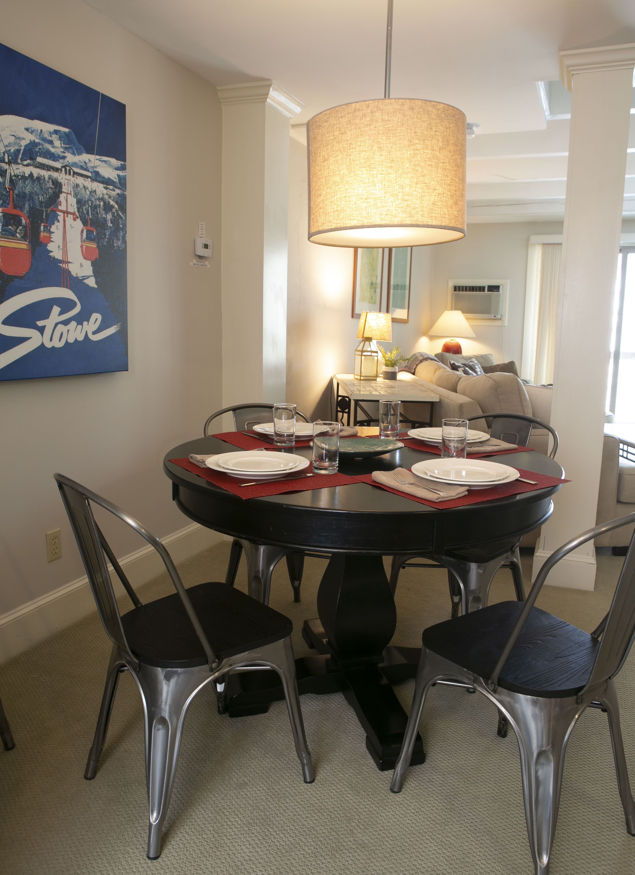 A dining area with a round table, chairs, and a hanging lamp.