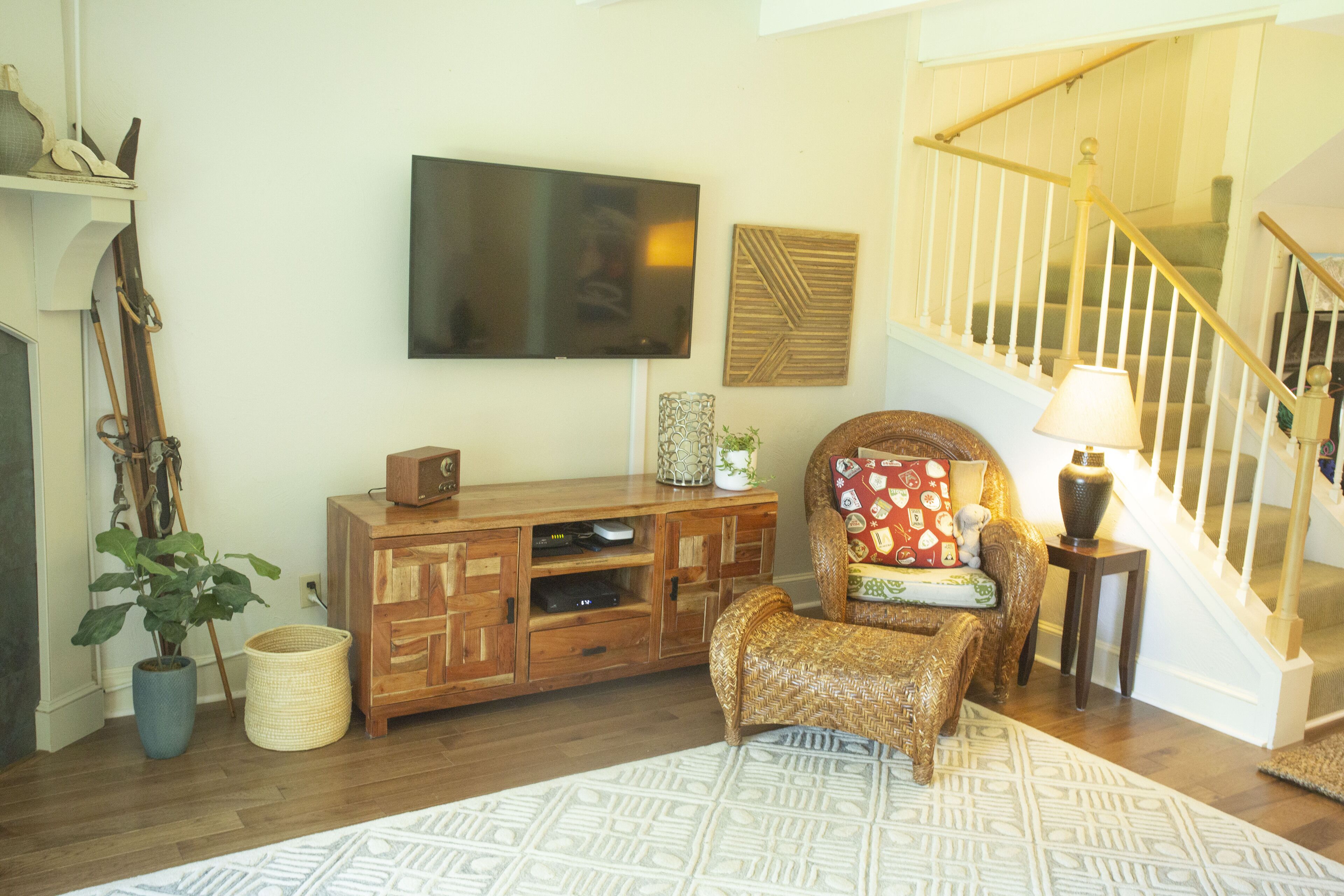 Una sala de estar con un mueble de entretenimiento de madera, un televisor, un sillón de mimbre, un tapete estampado y una escalera.