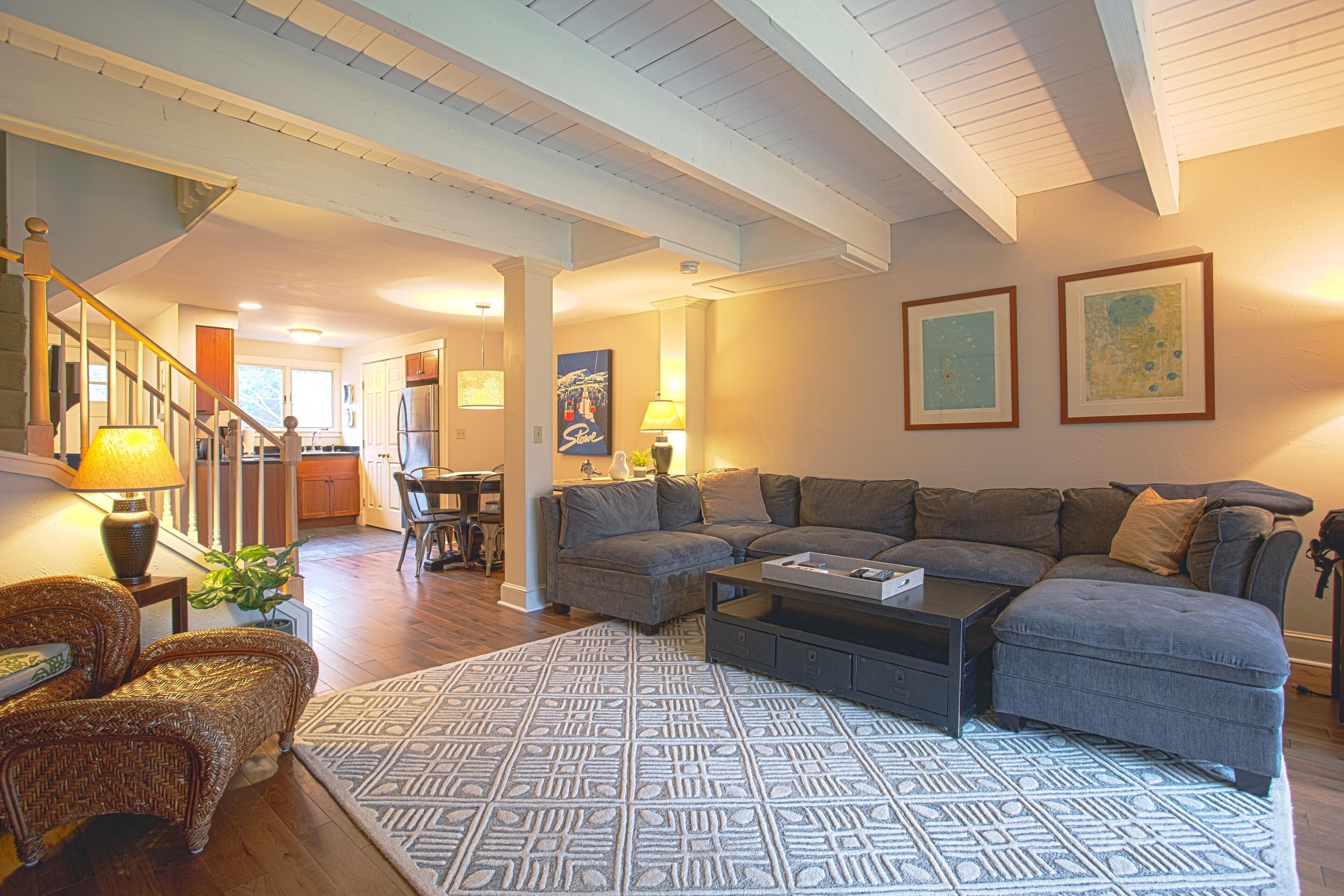 A spacious living room with a large sectional sofa, a patterned rug, and a dining area in the background.