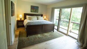A bedroom with a large bed, two bedside tables with lamps, a window with curtains, and a view of greenery outside. - Topnotch Resort, Stowe. Luxury 2/2 Resort Home just steps from the Spa.  (Stowe)