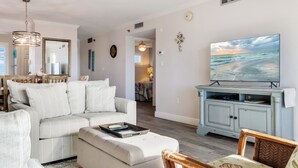 Una sala de estar con un sofá, un reposapiés y un televisor sobre un mueble.