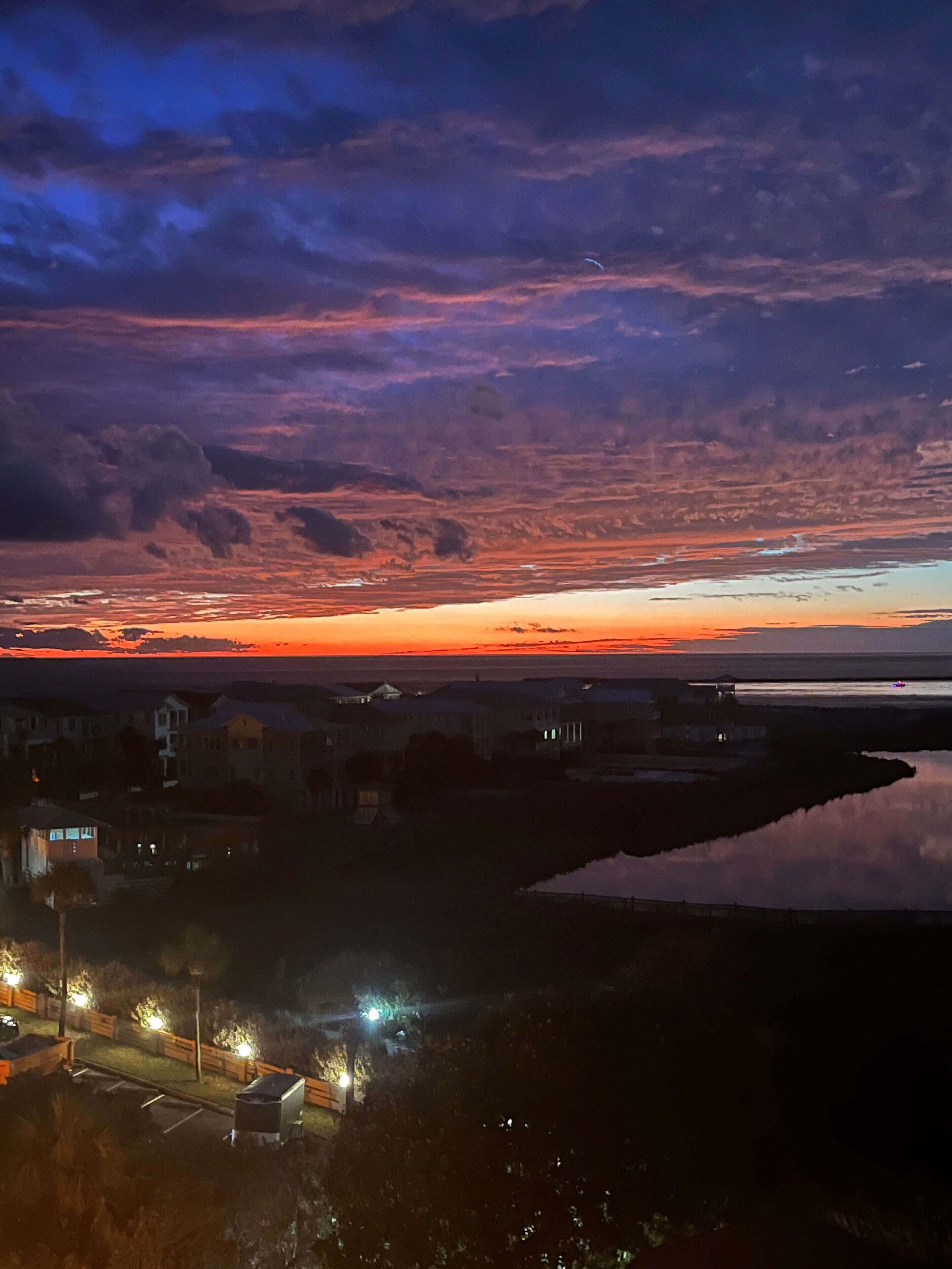 Un coucher de soleil sur une zone résidentielle, avec des maisons et une étendue d’eau.