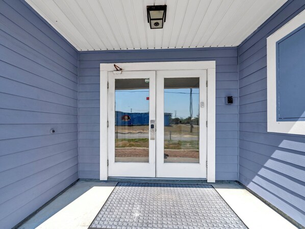 A house entrance with a white door, a small porch area, and a clear view of the driveway and surrounding landscape.