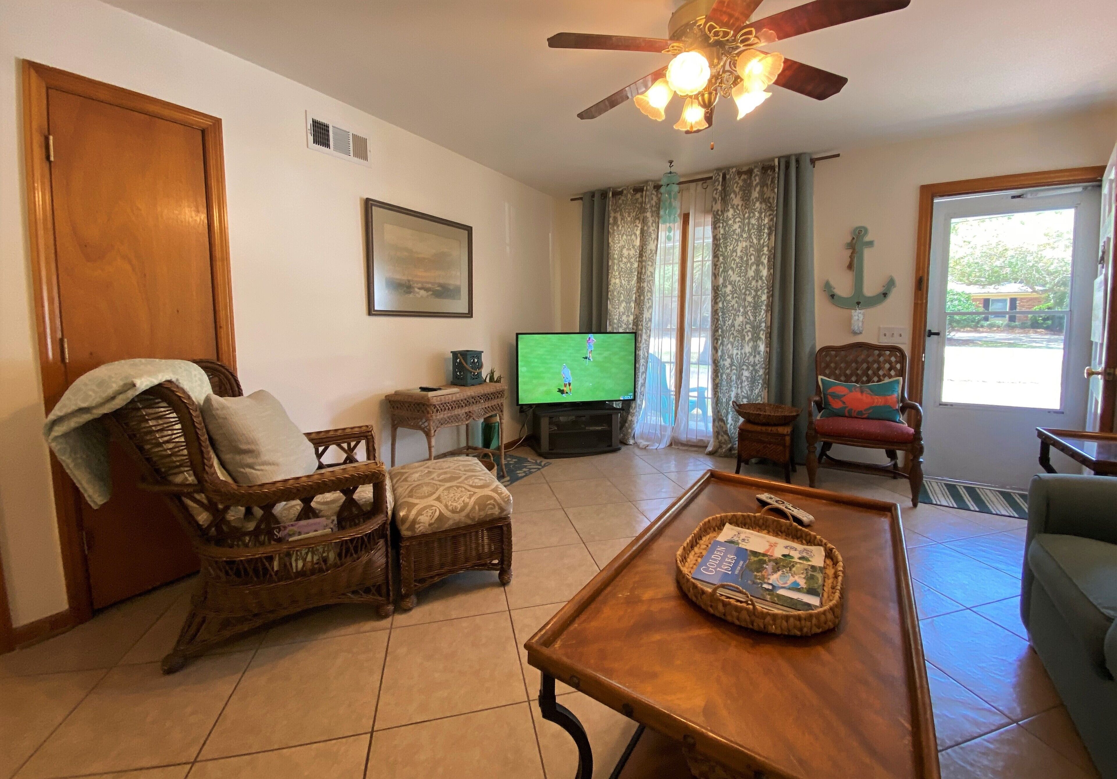 A living room with a television, wicker furniture, a wooden coffee table, and a ceiling fan.
