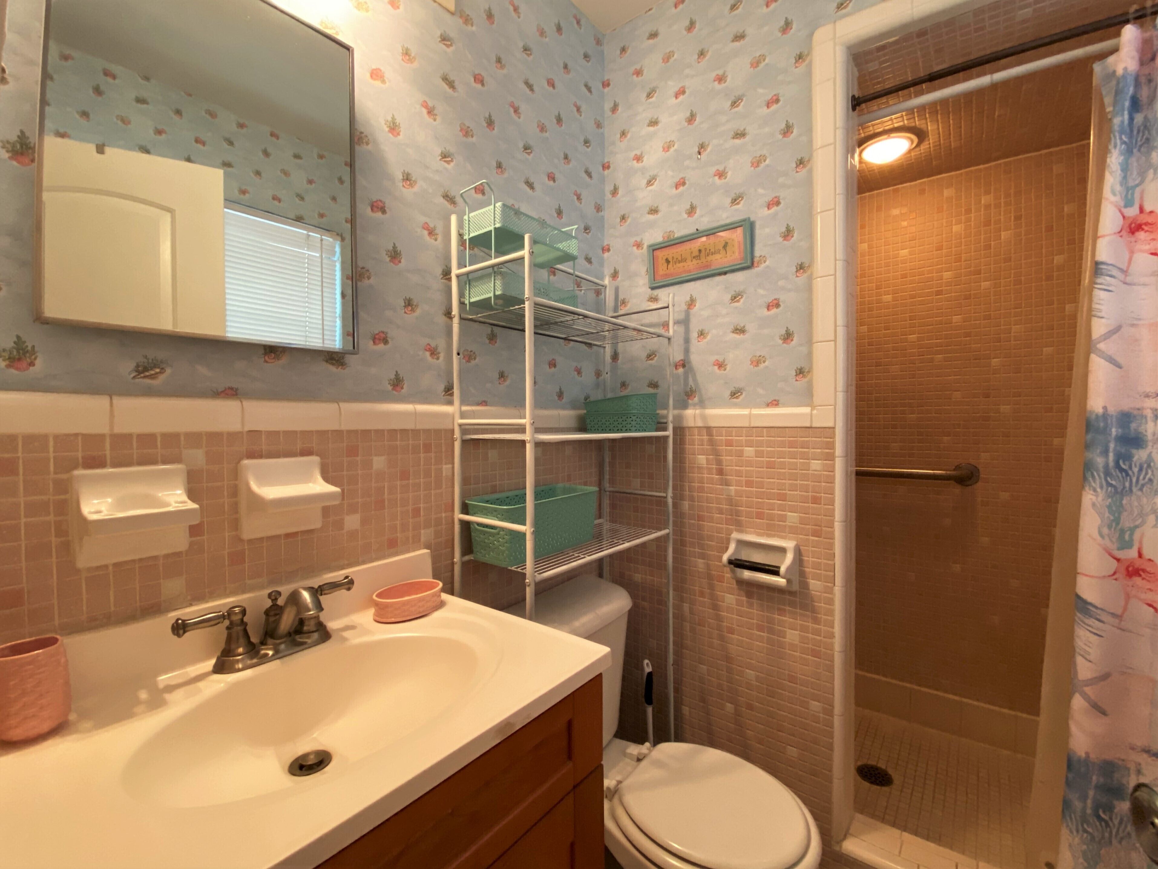 Un baño con un lavabo blanco, inodoro, ducha con cortina y repisas con cestas.