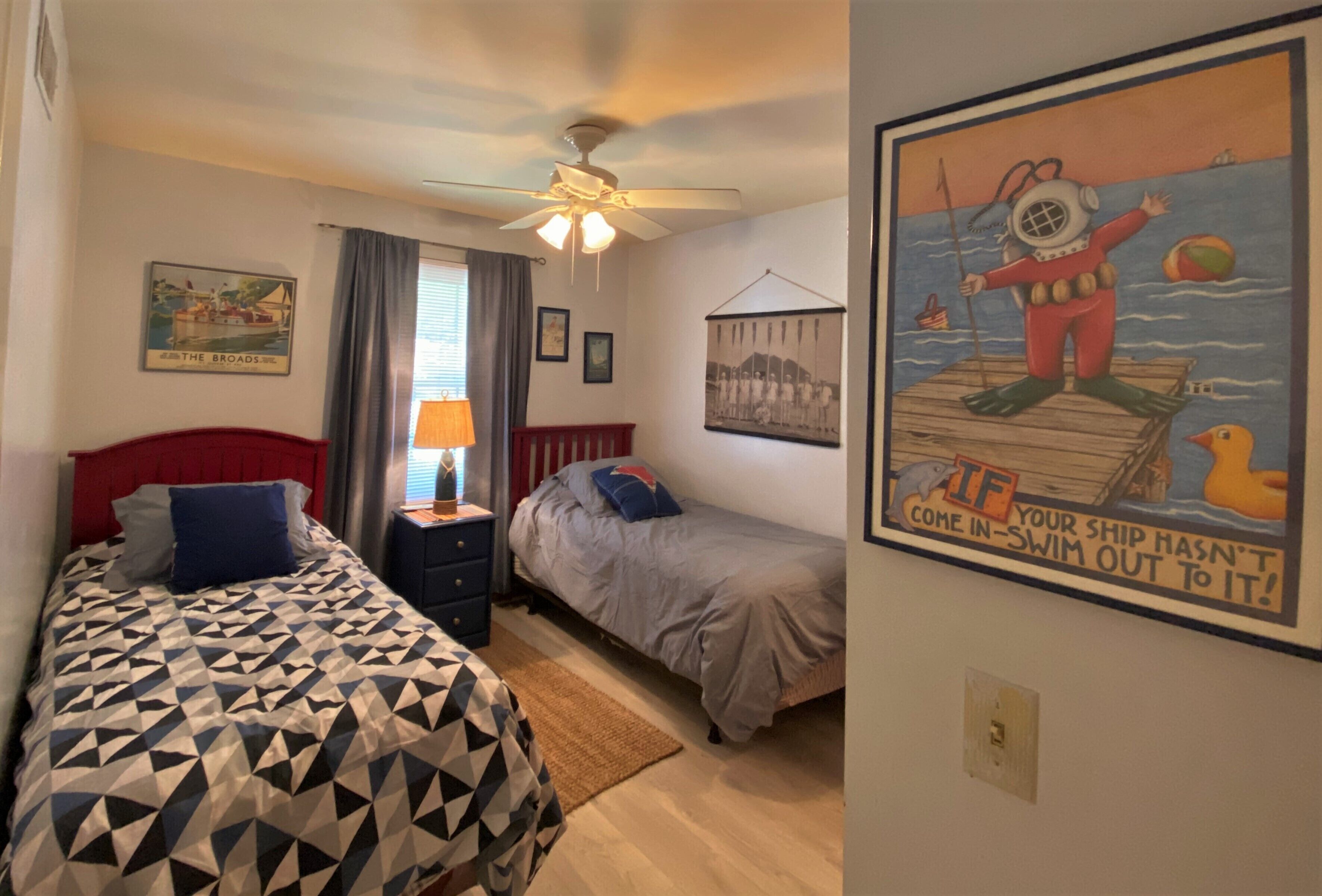 Quarto com duas camas, um ventilador de teto e um cartaz na parede.