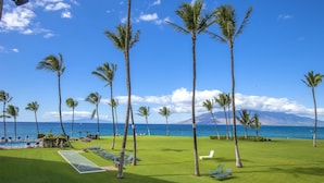 A golf course with a pool, palm trees, and a view of the ocean. - Oceanfront Retreat | Split A/C | Pool | Walk to Beach & Dining (KIHEI)