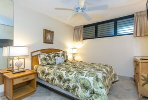 Un dormitorio con cama, lámparas de noche, ventilador de techo, ventana con cortinas y mesita de noche de madera.