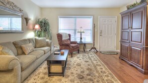 A living room with a sofa, armchair, coffee table, lamp, potted plant, and a cabinet. - Colonial Crest 107 - Great location! - You can walk to town! (Pigeon Forge)