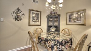 A dining room with a round table, four chairs, a chandelier, and three framed pictures on the wall. - Colonial Crest 107 - Great location! - You can walk to town! (Pigeon Forge)