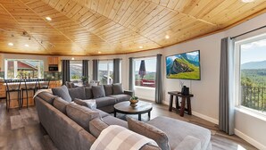 Un'ampia zona giorno con soffitto in legno, un divano grande, un tavolino da caffè e un televisore fissato alla parete.
