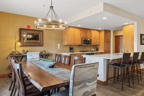 A modern kitchen with wooden cabinets, a central island with bar stools, and a chandelier. - Luxury Ski-In/Ski-Out Keystone Condo w/ Private Balconies for Mountain Views (Keystone)