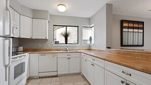 Une cuisine moderne avec des meubles blancs, un plan de travail en granit et une fenêtre donnant sur la verdure.