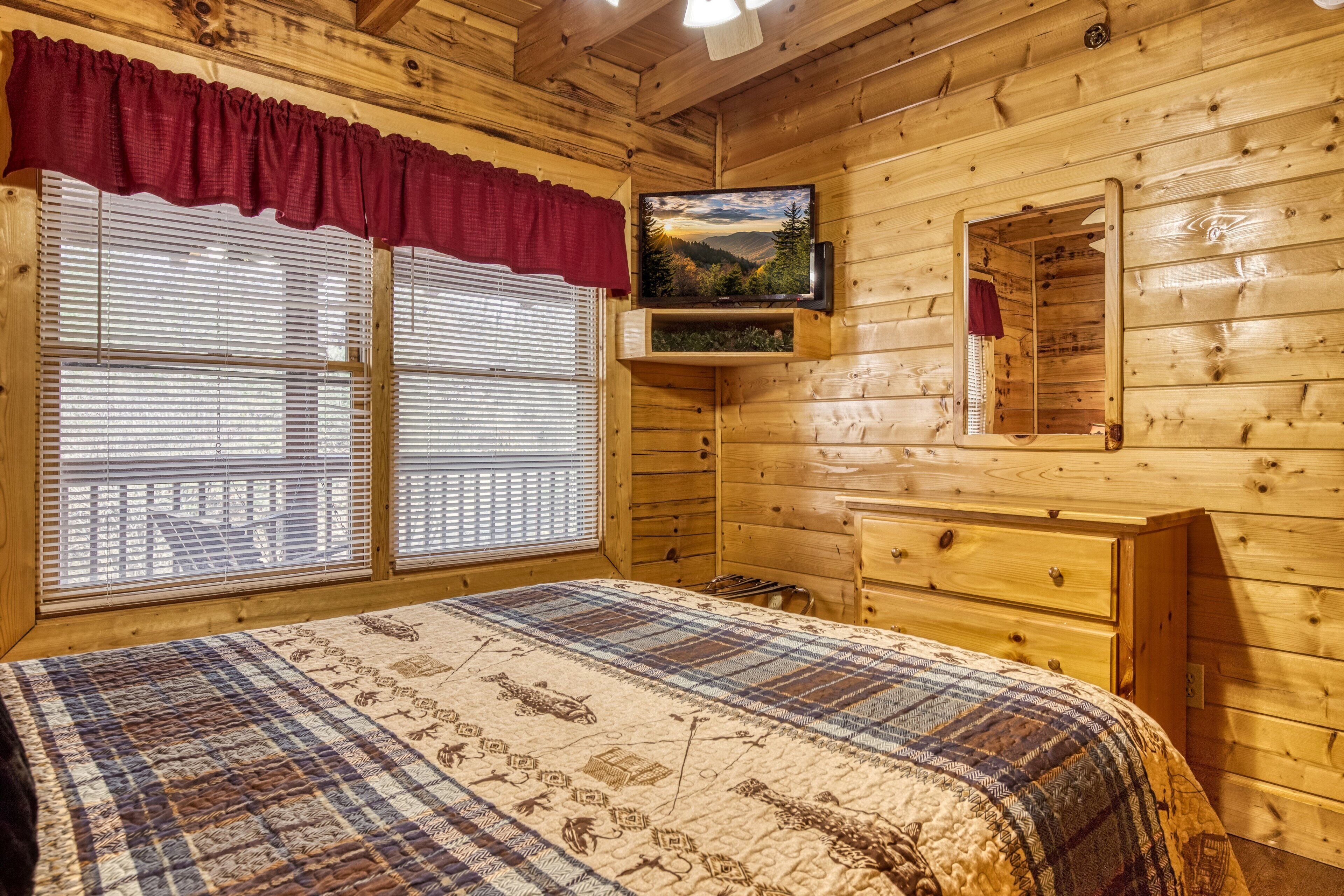 A wooden cabin room with a bed, a television, and a window with blinds.