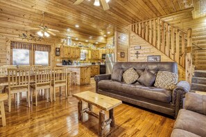 A wooden interior with a dining area, a sofa, and a staircase.