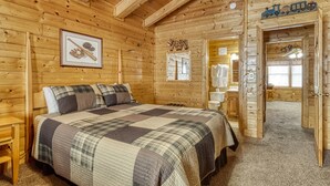 Una habitación tipo cabaña de madera con una cama grande, techo de madera y una puerta que da a un baño.
