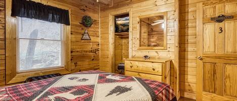 A wooden cabin bedroom with a bed, dresser, and a mirror.