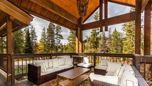 A covered outdoor seating area with a wooden ceiling, wicker furniture, and a view of a forest. - Great for Big Groups, Mile from Lifts, High End Finishes, Huge Deck, Hot Tub (Keystone)