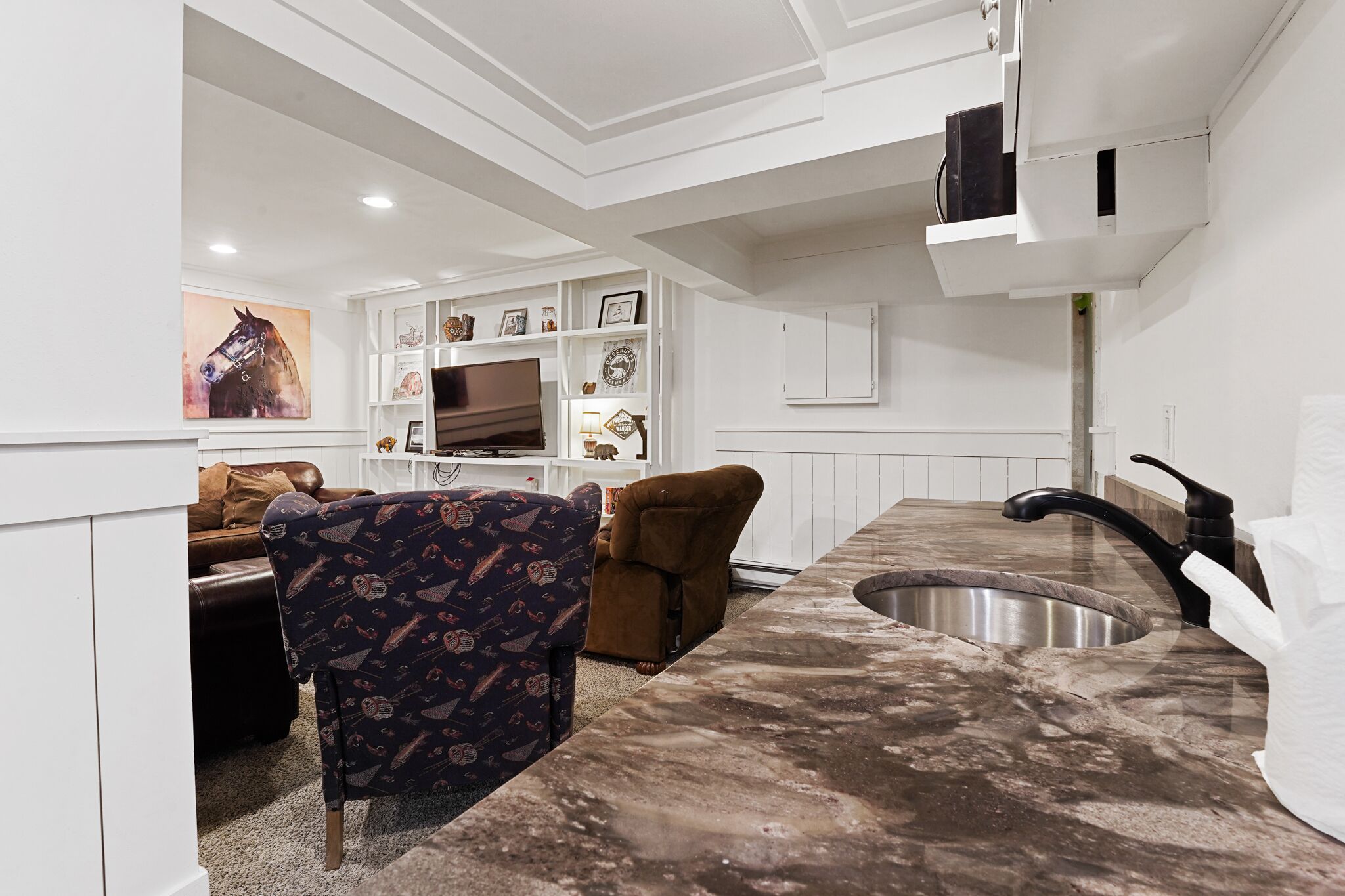 Una cocina moderna con encimera de mármol, pileta integrada y televisor sobre un mueble blanco.