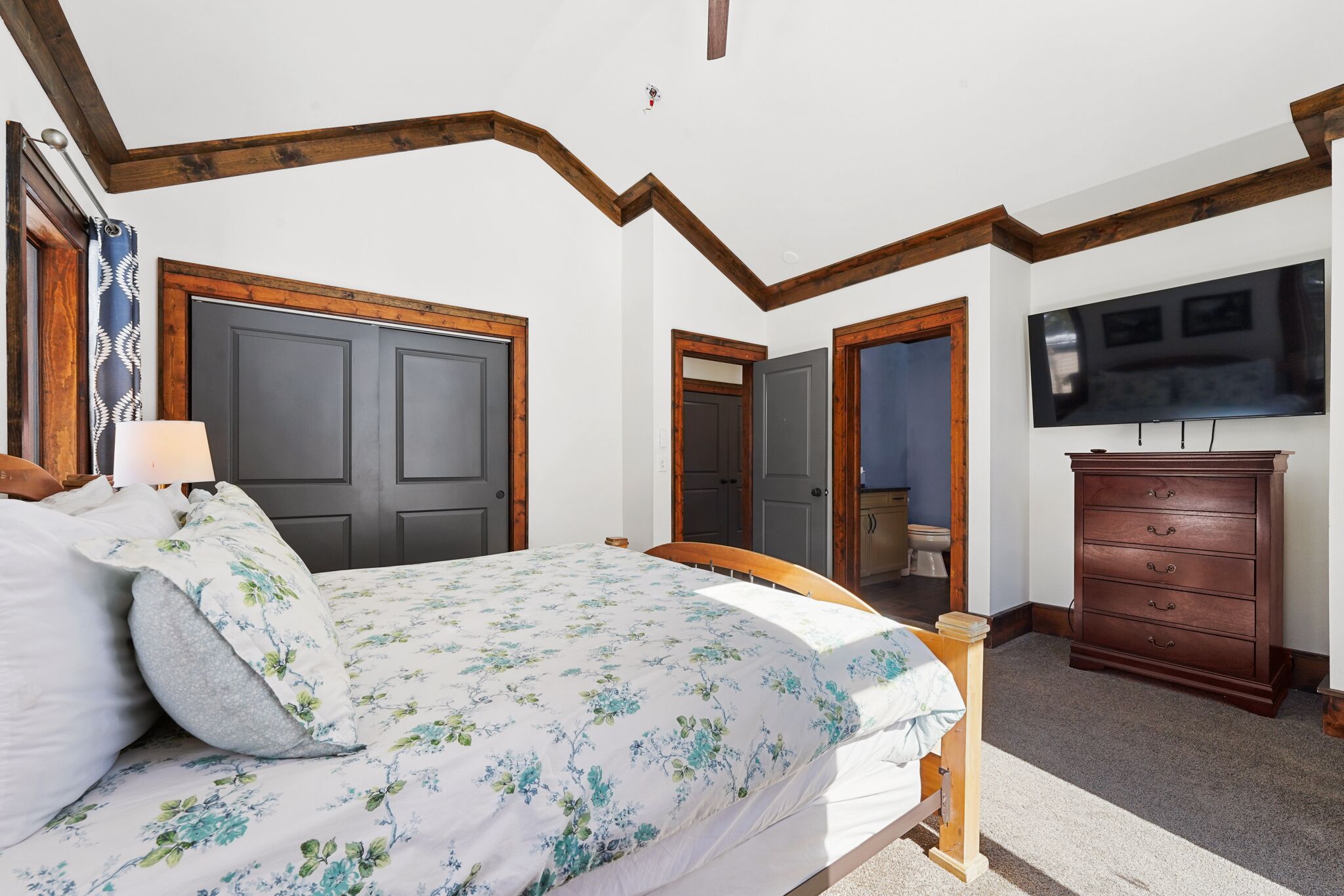 A bedroom with a bed, wooden headboard, a dresser, and a television on the wall.