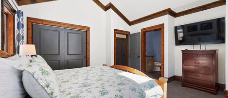 A bedroom with a bed, wooden headboard, a dresser, and a television on the wall.