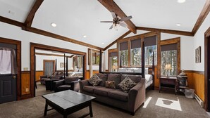 A spacious living room with a large couch, a coffee table, and a fireplace. There are large windows providing natural light and a view of the outdoors. - Great for Big Groups, Mile from Lifts, High End Finishes, Huge Deck, Hot Tub (Keystone)