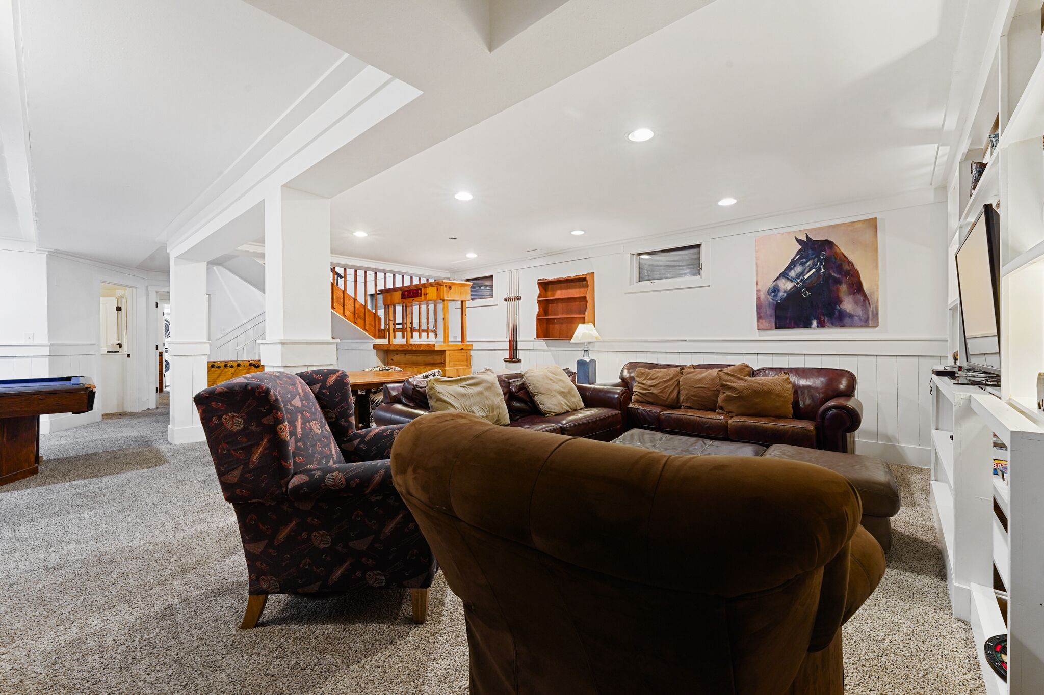 A spacious living room with a pool table, a brown leather sofa, and a staircase leading to an upper level.