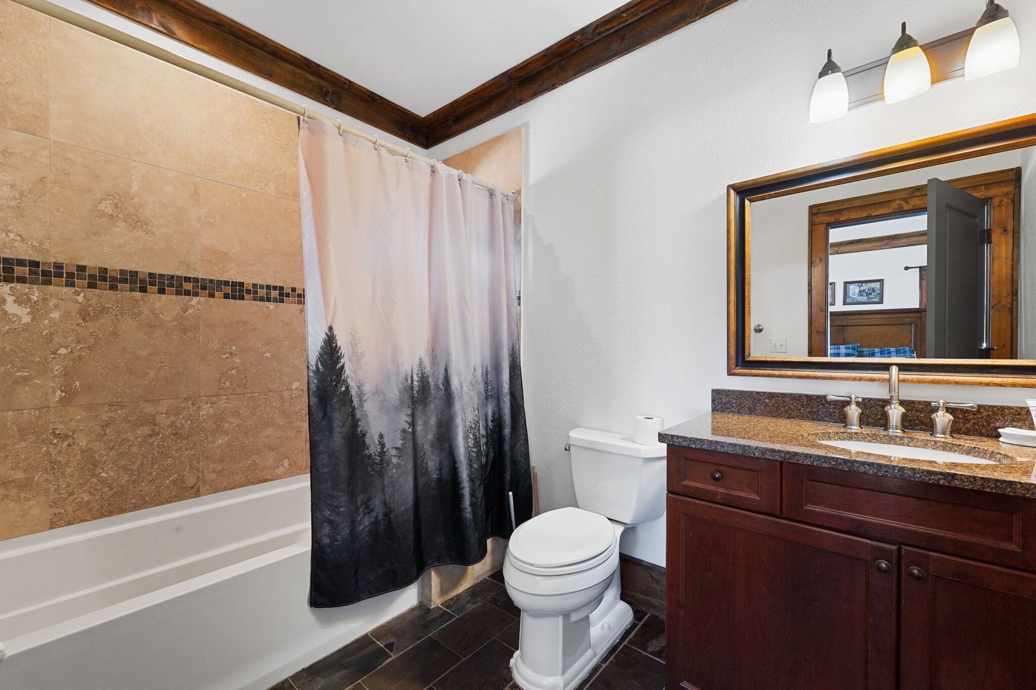 A bathroom with a shower curtain, toilet, vanity, and a large mirror.