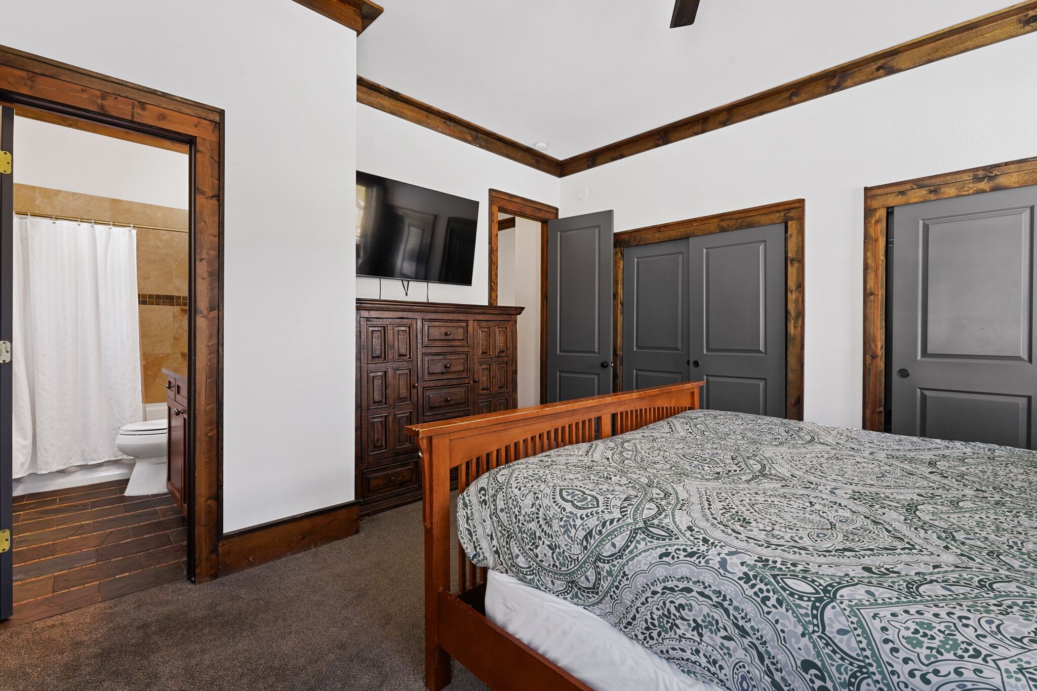 A bedroom with a wooden bed, a TV mounted on the wall, and a wardrobe.