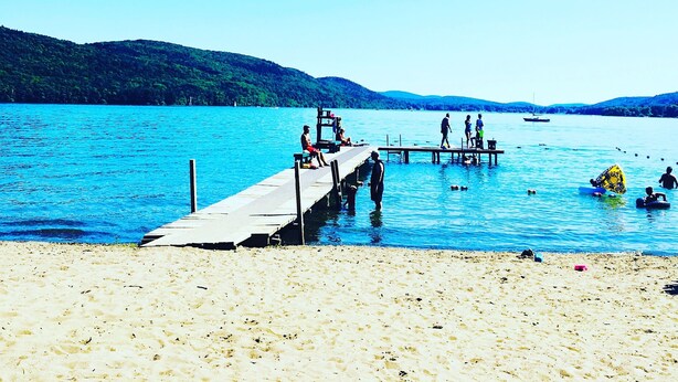 Une plage avec une jetée en bois qui s’avance dans l’eau, où l’on voit des gens se promener et s’asseoir.