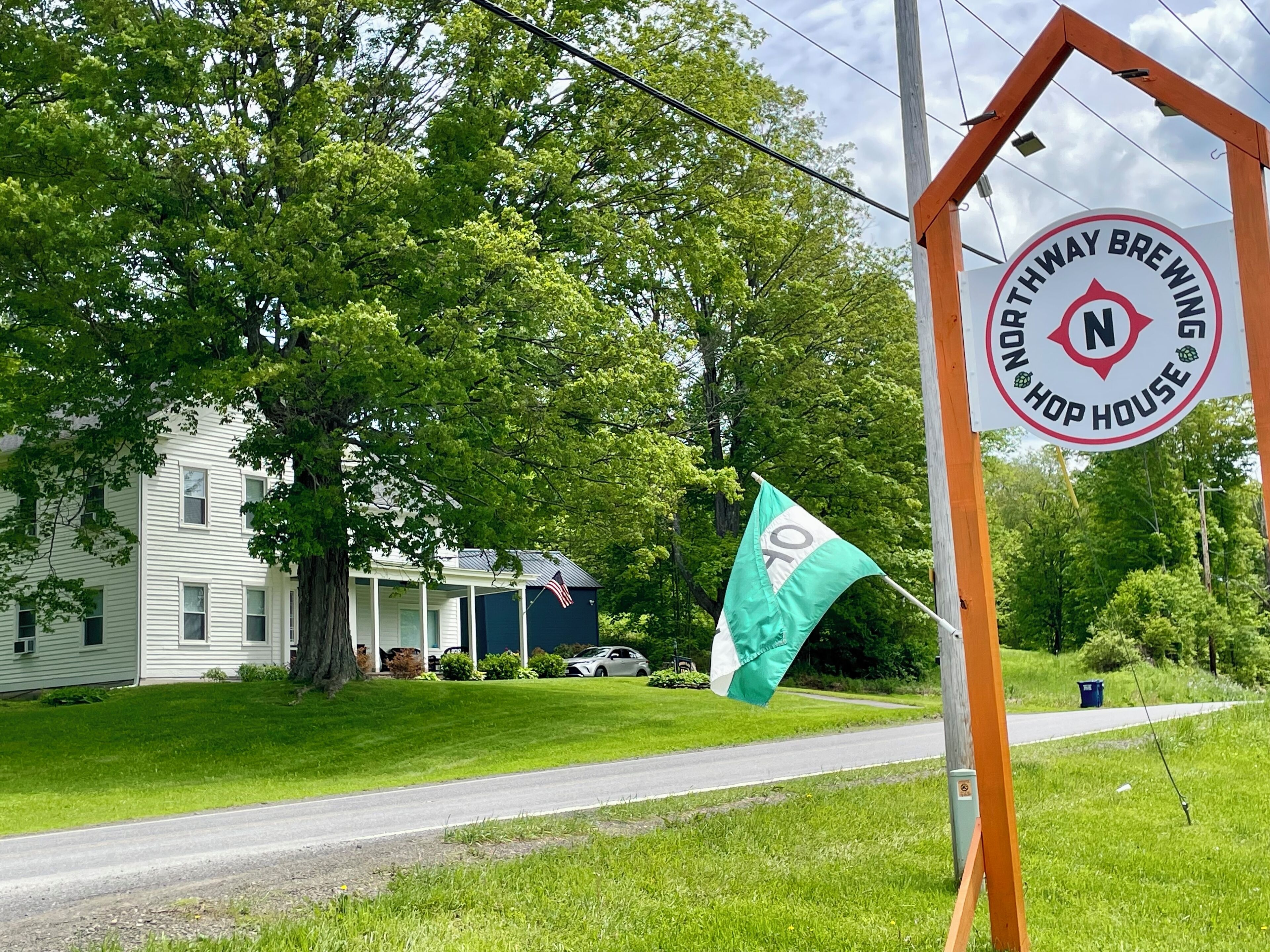 A sign for Northway Brewing Hop House with a green flag and a white building in the background.