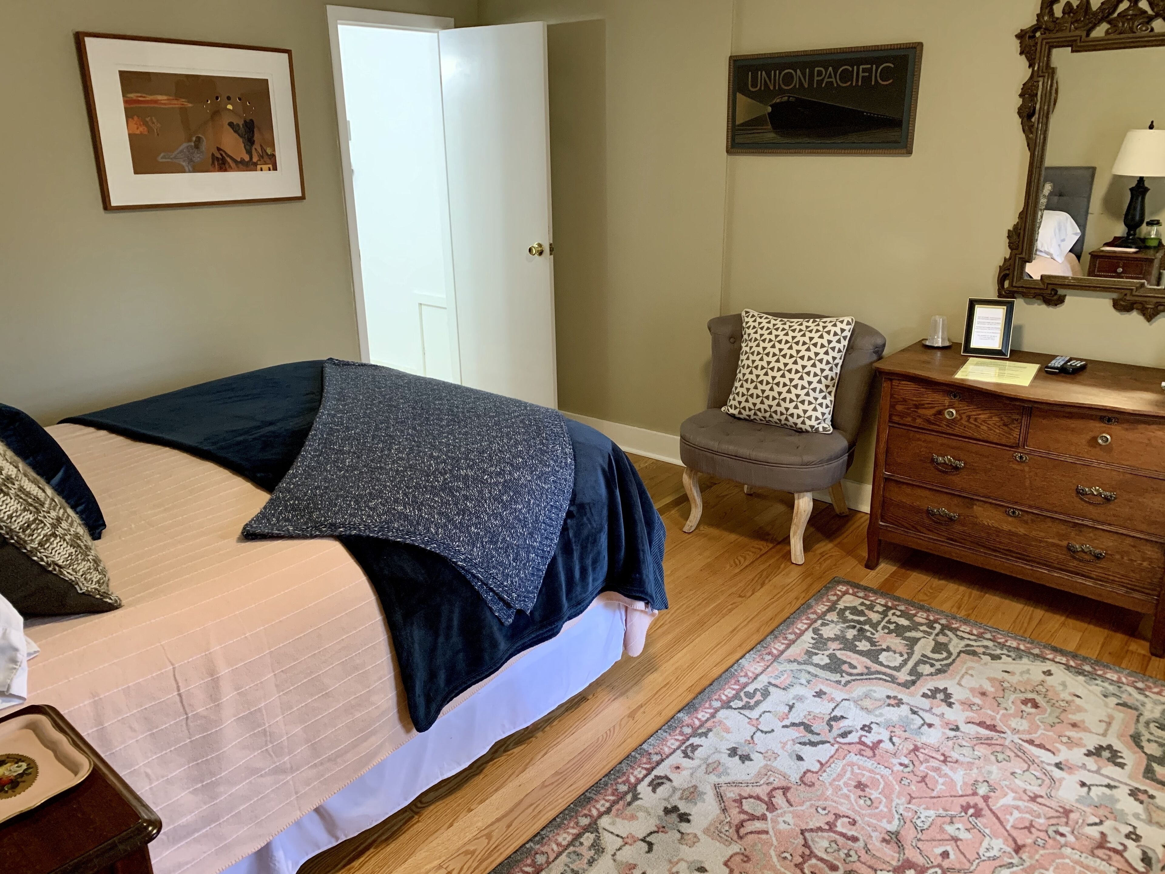 A bedroom with a bed, a chair, a dresser, a rug, and a door.