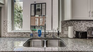 Una cocina moderna con un lavamanos doble, una ventana con vistas a árboles y un salpicadero con diseño de mosaico.
