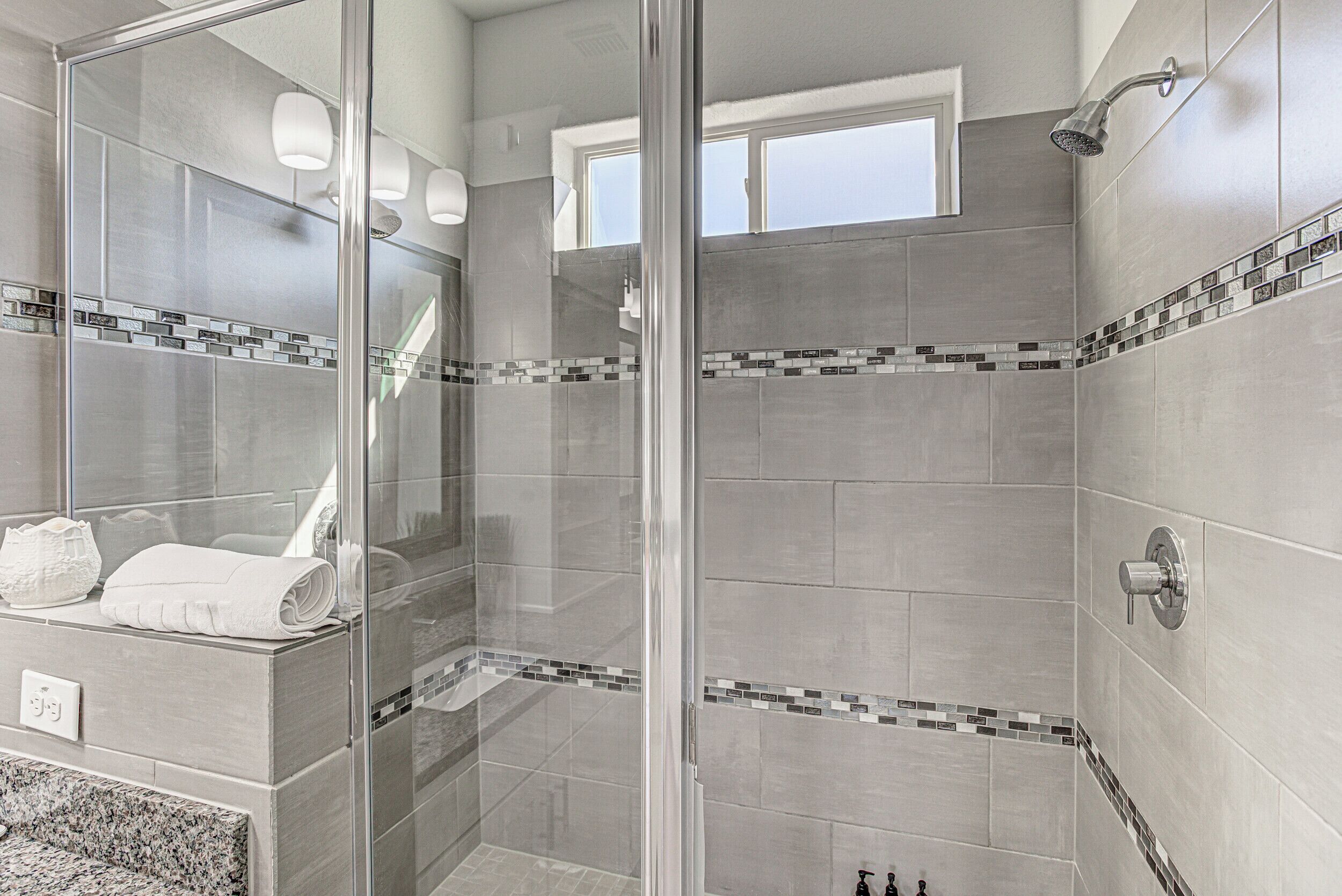 Een moderne badkamer met een douchecabine van glas, betegelde muren en een klein raam.