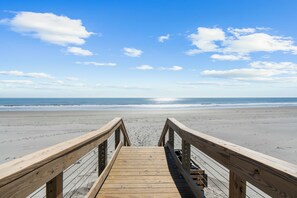 A wooden boardwalk leading to a beach with a clear sky and ocean.