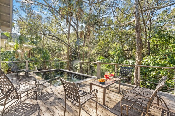 A wooden deck with metal chairs and a table, overlooking a pool and lush greenery.