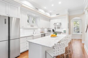 A modern kitchen with white cabinetry, stainless steel appliances, and a marble island with bar stools.