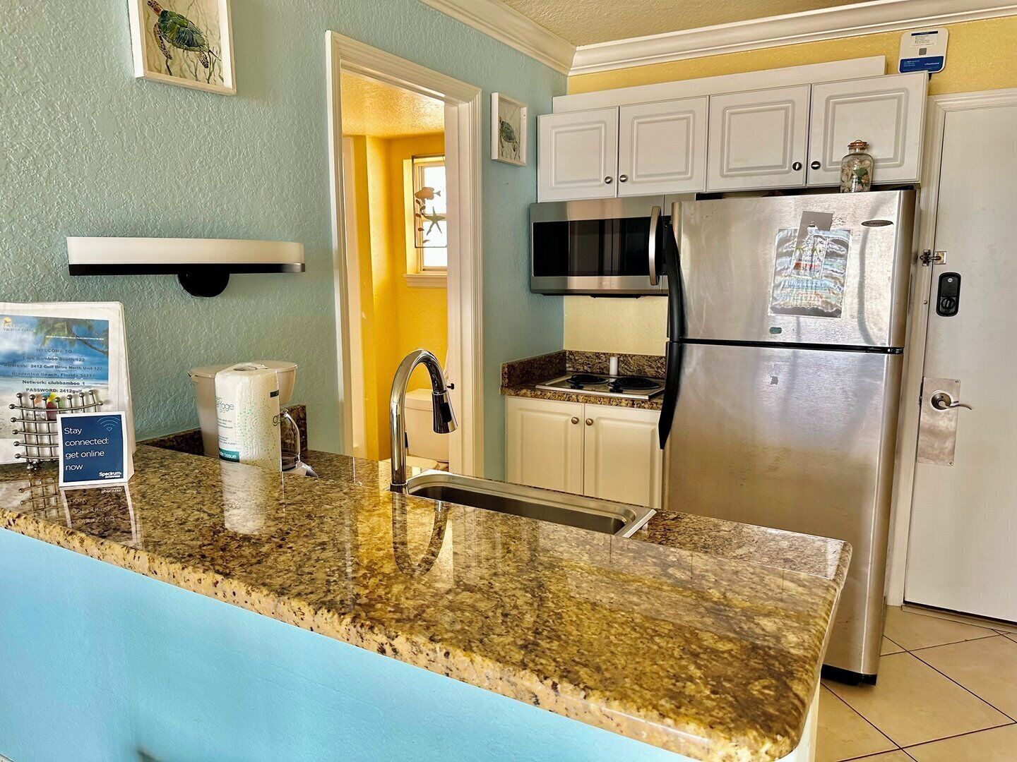 A kitchen with a granite countertop, stainless steel refrigerator, and white cabinets.