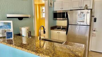 A kitchen with a granite countertop, stainless steel refrigerator, and white cabinets.