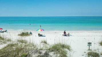 Une plage de sable blanc, quelques parasols et un panneau.
